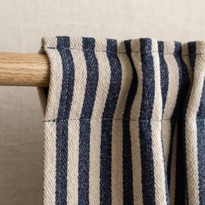 Puede incluir: Primer plano de un panel de cortina a rayas en azul marino y beige. La tela está drapeada sobre una barra de madera. Las rayas verticales crean un aspecto clásico y texturizado, adecuado para la decoración del hogar.