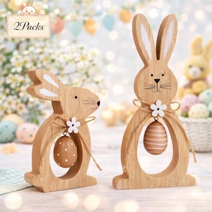 May include: Two wooden Easter bunny decorations. The bunnies are light brown with white accents on the ears. Each bunny has a decorative egg hanging from a twine bow. The image includes the text "2 Packs".