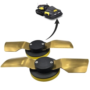 Op de afbeelding: Twee goudkleurige metalen maaimesjes met zwarte ronde naven en gele basissen. Elk mes heeft twee zilveren schroeven op de naaf en de tekst "THIS SIDE FACING GRASS" in het metaal gedrukt. Een kleine robotmaaier is hierboven afgebeeld.