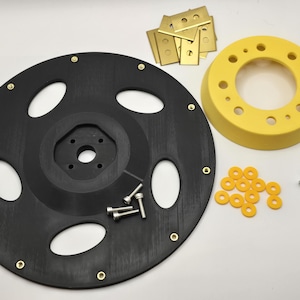 May include: A large black circular component with four oval cutouts and brass inserts, a yellow ring with multiple holes, several small brass rectangular plates, yellow washers, and a collection of silver metal bolts and screws.
