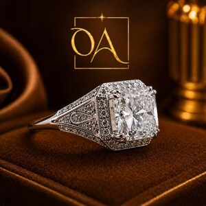 Puede incluir: Un deslumbrante anillo de diamantes con un diamante central de talla cuadrada y detalles intrincados. El anillo presenta peque&ntilde;os diamantes y un engaste plateado. Se muestra sobre una superficie marr&oacute;n, con un logotipo dorado.