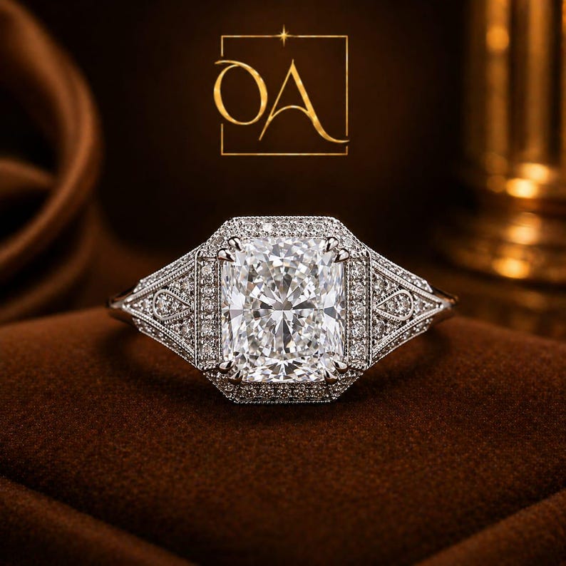 Puede incluir: Un anillo de diamantes de talla rectangular con un halo de diamantes m&aacute;s peque&ntilde;os. El anillo presenta un dise&ntilde;o intrincado en la banda y alrededor de la piedra central. El anillo est&aacute; sobre una superficie marr&oacute;n, con las letras "OA" en un cuadrado dorado en el fondo.