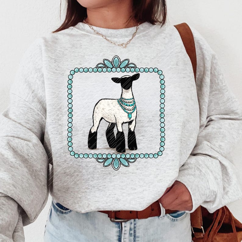 May include: A light grey sweatshirt with a graphic of a sheep wearing a turquoise necklace, framed by a turquoise beaded border. The sheep has a black head and legs. The sweatshirt has long sleeves.