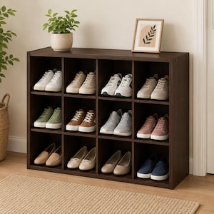 May include: A dark brown shoe organizer with multiple compartments, each holding a pair of shoes. The shoes vary in style and color, including sneakers, flats, and loafers. A small potted plant and framed artwork sit on top.