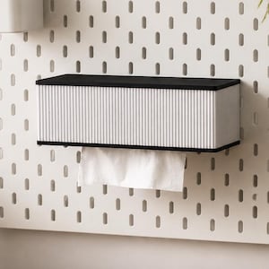 Pode incluir: Um painel perfurado branco com uma caixa de lenços preta e branca anexada. Um porta-canetas branco é montado acima da caixa de lenços. Um laptop, um pequeno bloco de madeira, um caderno e uma xícara estão na mesa de madeira.