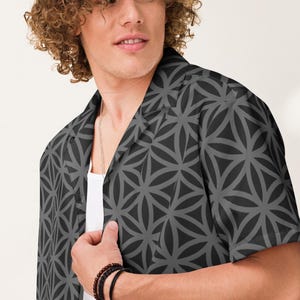 Op de afbeelding: Een shirt met korte mouwen en een geometrisch patroon in grijstinten. Het shirt is open, met daaronder een wit ondershirt. Het heeft een klassieke kraag en is gemaakt van een lichte stof. De stijl is casual en modern. Het patroon bestaat uit herhaalde vormen.