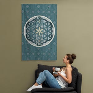 May include: A wall tapestry with a teal and white geometric design. The tapestry features a large circular emblem with a flower-like pattern in shades of blue and yellow. The background has a repeating pattern of teal lines.