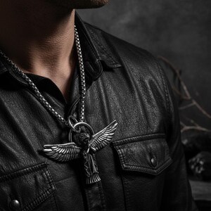 May include: Silver-toned angel pendant necklace. The pendant features an angel with outstretched wings and intricate detailing. The necklace is worn over a black leather jacket, creating a bold and stylish look. The chain is a linked design.