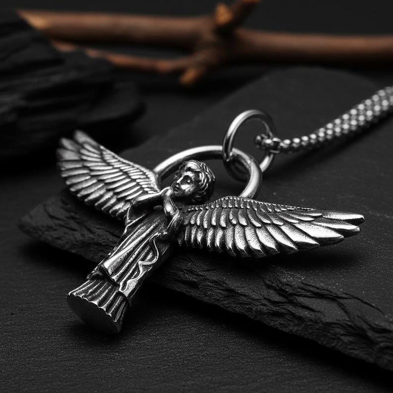 May include: A silver-colored angel pendant necklace. The pendant features an angel with outstretched wings and detailed feathering. The necklace has a chain with a small link pattern. The angel is attached to a circular bail.