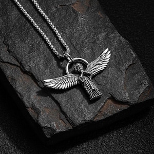 May include: Silver-toned angel pendant necklace. The pendant features an angel with outstretched wings, suspended from a chain. The necklace is displayed on a dark, textured surface, creating a striking contrast.