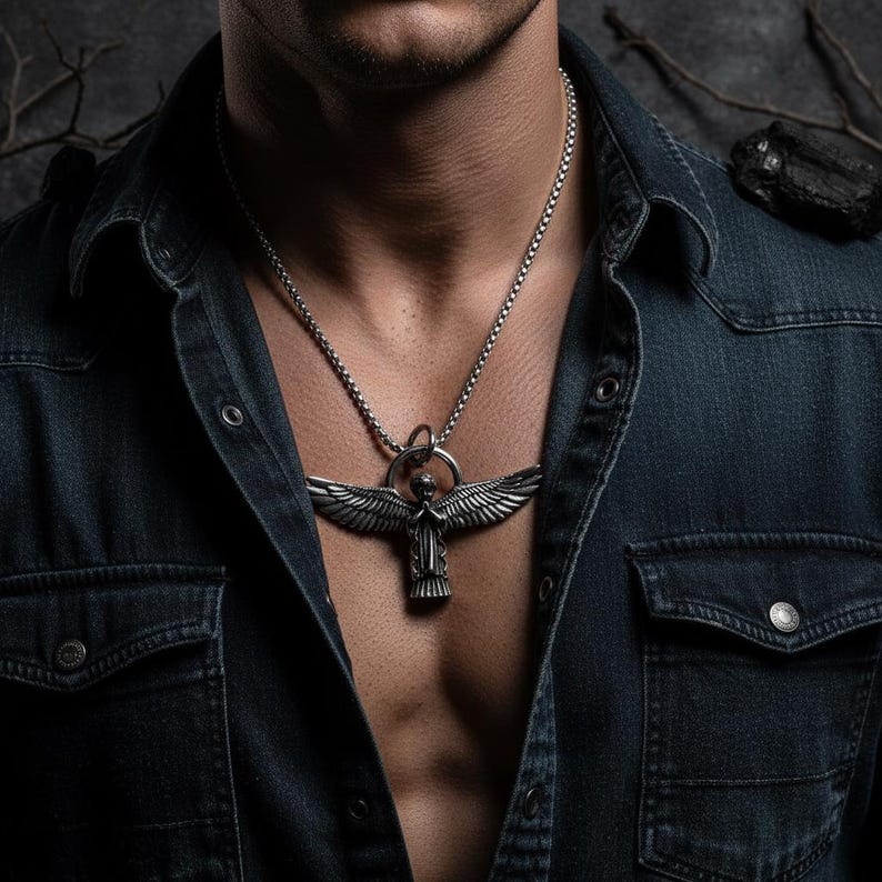 May include: A silver-toned pendant necklace featuring an angel with outstretched wings. The detailed pendant hangs from a chain necklace. The person in the image is wearing a dark blue denim shirt.