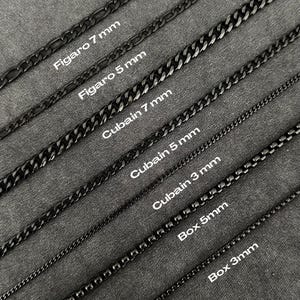 Può includere: Un assortimento di collane a catena in metallo nero in vari stili e larghezze, tra cui catene Figaro, Cubane e Box. L'immagine mostra le catene su uno sfondo grigio, con testo che indica il tipo di catena e la larghezza in mm.