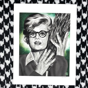 May include: A black and white illustration of a woman with glasses holding a broom. The artwork features a green background and is signed in the bottom right corner. The woman is wearing a sweater and a collared shirt.