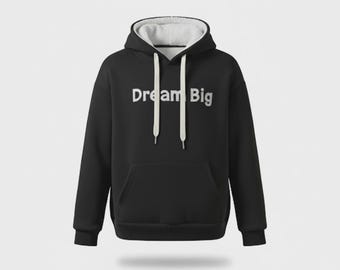 Könnte beinhalten: Schwarzer Kapuzenpullover mit weißem, fleecegefüttertem Kapuzen- und Kordelzug. Auf der Vorderseite befindet sich eine Kängurutasche und der Schriftzug "Dream Big" in weißen Blockbuchstaben.