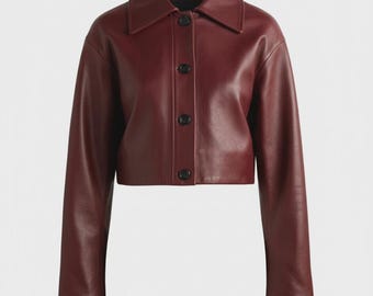 May include: A burgundy leather jacket with a collared neckline and long sleeves. The cropped jacket features a button-up front with three black buttons. The jacket is a solid color and has a smooth texture.