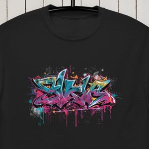 Könnte beinhalten: Schwarzes T-Shirt mit einem Graffiti-Design in Türkis, Pink und Gelb. Das Kunstwerk hat einen tropfenden Farbeffekt, der eine urbane Ästhetik erzeugt. Das T-Shirt hängt an einem schwarzen Kleiderbügel vor einem weißen Holzhintergrund.