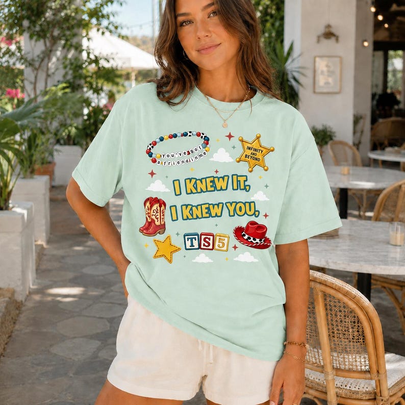 May include: A light green short-sleeve t-shirt featuring a graphic print with the text "I KNEW IT, I KNEW YOU," a beaded bracelet, a sheriff badge, red cowboy boots, a yellow star, "TS5" blocks, and a red cowboy hat with white trim.