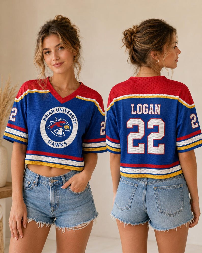 May include: Blue, red, and white cropped jersey with the text "Briar University Hawks" and the number "22". The jersey has a V-neck and is worn with denim shorts. The jersey has the name "Logan" on the back.