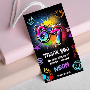 May include: A black gift tag with a white string. The tag features colorful graffiti-style art with the number "67" in the center. Text includes "Thank you" and "NEOM", with the date "October 20 | 2026".