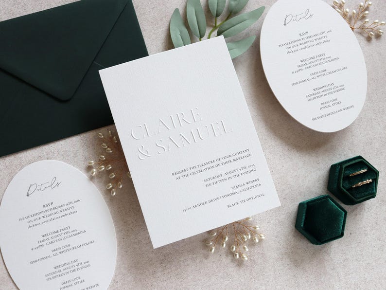 May include: Elegant wedding invitation suite featuring embossed text with the names "Claire & Samuel". Includes a dark green envelope, oval details cards, and a dark green velvet ring box. The invitation details the wedding date and location.