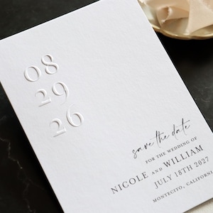 Może przedstawiać: Biała karta zaproszenia ślubnego z wytłoczonymi numerami i tekstem. Karta głosi "save the date" i zawiera imiona Nicole i William, datę 18 lipca 2027 r. oraz lokalizację Montecito w Kalifornii.