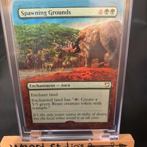 May include: A Magic: The Gathering card titled "Spawning Grounds" featuring a landscape with a large, furry beast. The card is in a protective case and displayed on a small wooden easel. The text "Weerd Studios 3" is written on the easel.