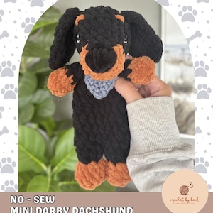 Puede incluir: Un juguete de peluche de perro salchicha tejido a ganchillo con hilo negro y marrón, con un pequeño parche triangular gris en el pecho y ojos oscuros. El texto dice: @crochet.by.beck, NO-SEW MINI DARBY DACHSHUND, DIGITAL DOWNLOAD CROCHET PATTERN.