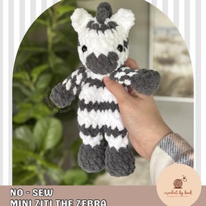 Peut inclure: Un jouet zèbre crocheté à la main en noir, blanc et gris. Le zèbre a un corps rayé, un museau gris et de petits yeux noirs. Le texte "NO - SEW MINI ZITI THE ZEBRA DIGITAL DOWNLOAD CROCHET PATTERN" est visible.