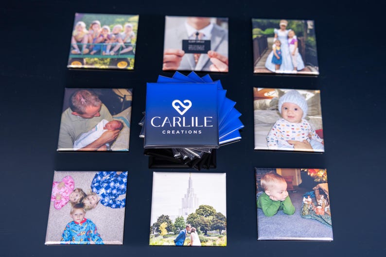 May include: A collection of square magnets featuring various photographs, including family portraits, a baby, and a wedding scene. A stack of blue business cards with the "Carlile Creations" logo is in the center. The magnets are arranged on a dark surface.