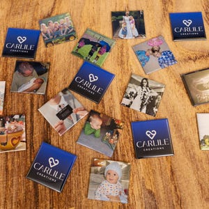 May include: A collection of square magnets with various images and the text "CARLILE CREATIONS" on a blue background. The images include photos of people, events, and a logo. The magnets are arranged on a wooden surface.
