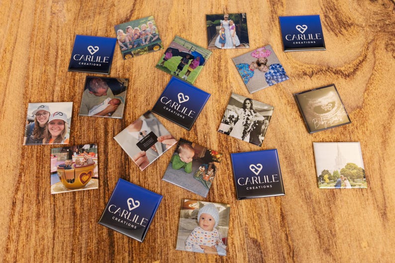 May include: A collection of square magnets with various images and the text "CARLILE CREATIONS" on a blue background. The images include photos of people, events, and a logo. The magnets are arranged on a wooden surface.