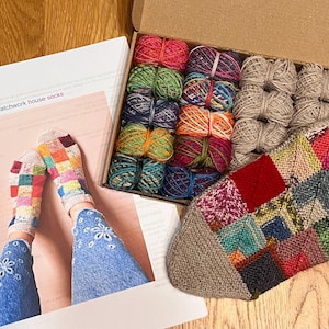Peut inclure: Un kit de création avec des pelotes de laine colorées et une chaussette patchwork partiellement tricotée. Le kit comprend une boîte de fils de différentes couleurs et un patron pour des chaussettes patchwork. Les chaussettes sont multicolores.