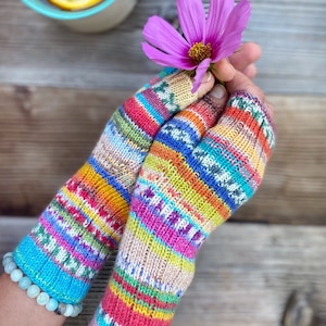 May include: A pair of colorful fingerless gloves with a striped pattern. The gloves are made of a soft, knitted fabric and are held in a person's hands. A pink flower is also being held in the hands.