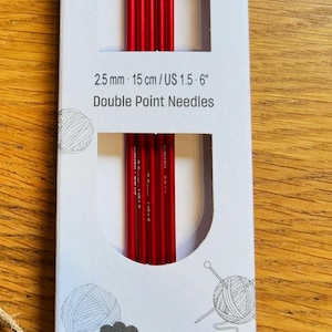 May include: A package of Knit Pro ZING double point needles. The package is white with red text and illustrations of yarn and sheep. The needles are red and measure 2.5 mm and 6 inches.