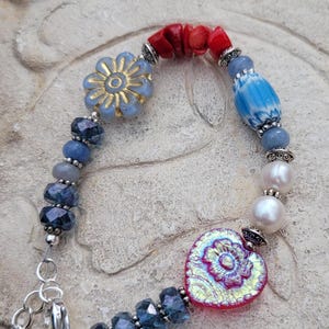 May include: A blue and red beaded bracelet with a heart-shaped charm, a flower charm, and a pearl bead.