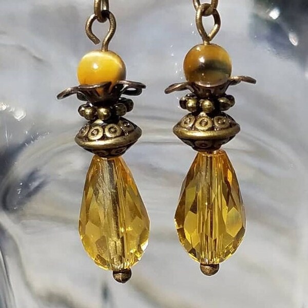 Goldenrod yellow beveled crystal teardrop dangle earrings topped with antique brass and gold-blue Tiger Eye beads. Antique brass ear wires.