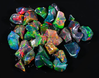 May include: A collection of rough-cut black opal gemstones. The opals display a vibrant play-of-color, with flashes of red, green, blue, and yellow. The gemstones are irregularly shaped and vary in size, set against a black background.