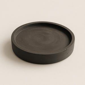May include: A round, dark gray concrete tray with a raised edge. The tray is circular and has a matte finish. The product is designed for decorative or functional use.