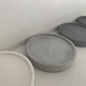 May include: Four round concrete coasters in different sizes. The coasters are grey and white.
