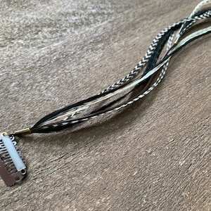 May include: A set of black and white feathers with a brown feather attached to a silver hair clip.