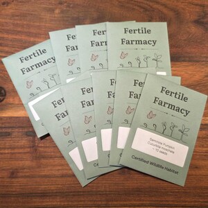 May include: A collection of seed packets with the text "Fertile Farmacy" in a light green color. The packets feature illustrations of butterflies and sprouts. One packet has a label that reads "Seminole Pumpkin Cucurbita moschata - 10 seeds."