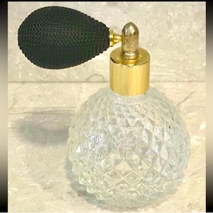 May include: A vintage perfume bottle with a clear, diamond-patterned glass body and a black bulb atomizer. The bottle has a gold-colored metal collar and nozzle. The atomizer is black and pear-shaped.