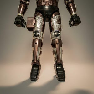 Może przedstawiać: Figurka akcji vintage robota, z metalicznym brązowym i srebrnym schematem kolor&oacute;w. Figurka ma czarne akcenty na dłoniach, stopach i g&oacute;rnej części ciała. Nogi i ramiona mają skomplikowane detale mechaniczne.