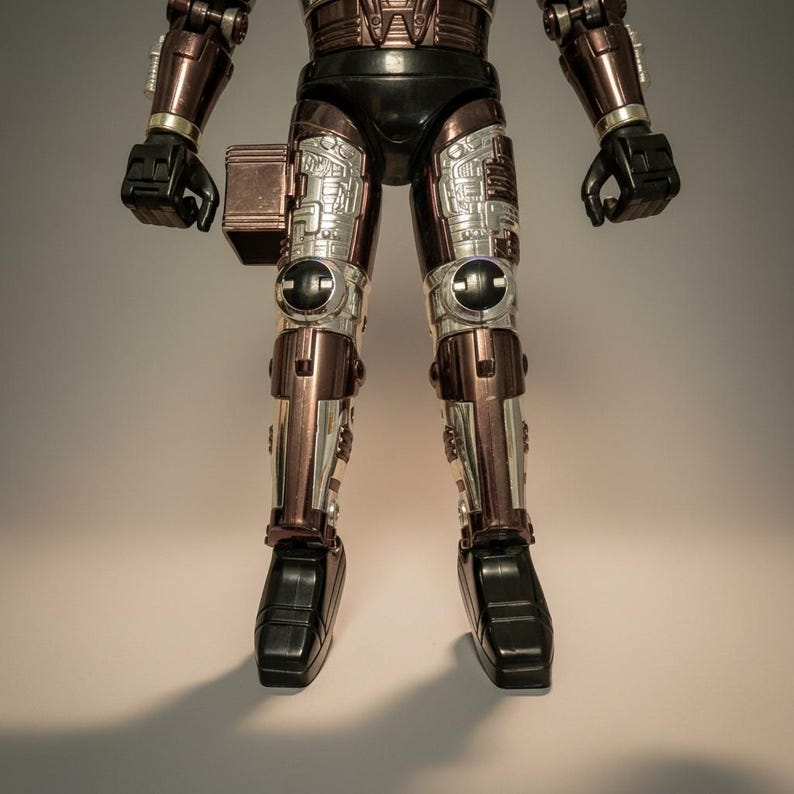 Może przedstawiać: Figurka akcji vintage robota, z metalicznym brązowym i srebrnym schematem kolor&oacute;w. Figurka ma czarne akcenty na dłoniach, stopach i g&oacute;rnej części ciała. Nogi i ramiona mają skomplikowane detale mechaniczne.