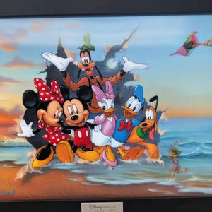 May include: Framed artwork featuring Disney characters Mickey Mouse, Minnie Mouse, Donald Duck, Daisy Duck, Goofy, and Pluto on a beach. The colorful scene includes a kite and a child running in the water, set against a sunset sky.