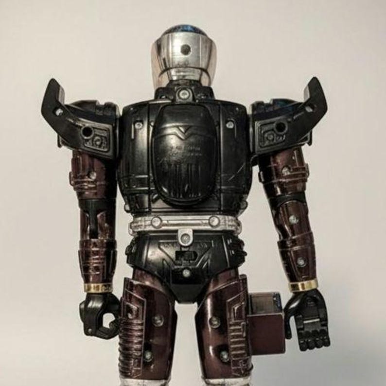 Może przedstawiać: Figurka robota w stylu vintage ze srebrną głową, czarnym tułowiem i bordowymi ramionami i nogami. Robot ma przeguby, szczeg&oacute;łową płytę piersiową i złote akcenty. Figurka to zabawka kolekcjonerska.