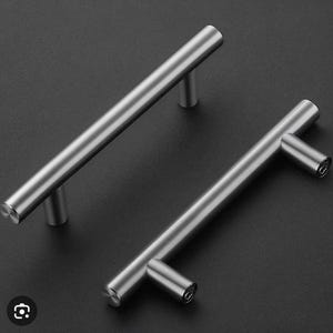 Può includere: Due maniglie per mobili in nichel spazzolato con una barra cilindrica e due montanti cilindrici. L'hardware è mostrato su uno sfondo scuro. Le maniglie sono progettate per una facile installazione e un'estetica moderna.