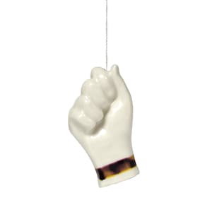 May include: White ceramic light pull shaped like a hand with a closed fist. The hand has a brown and purple band around the wrist.