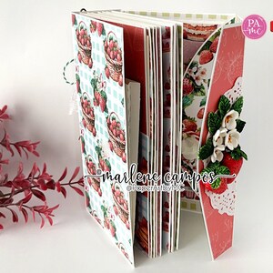 May include: A handmade scrapbook album with a strawberry theme. The pages feature a repeating pattern of strawberry baskets on a blue and white checkered background. The album is decorated with paper strawberries and flowers.