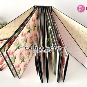 May include: A black and white floral patterned scrapbook with a green ribbon. The scrapbook is open to reveal multiple pages with different floral patterns. The text "marlene campos" and "@PaperArtbyMC" is written on the inside of the scrapbook.